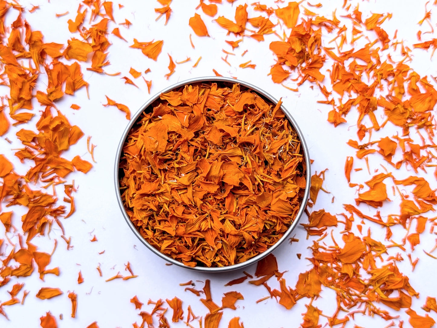 Dried orange marigold edible flowers in recyclable metal container on a white background